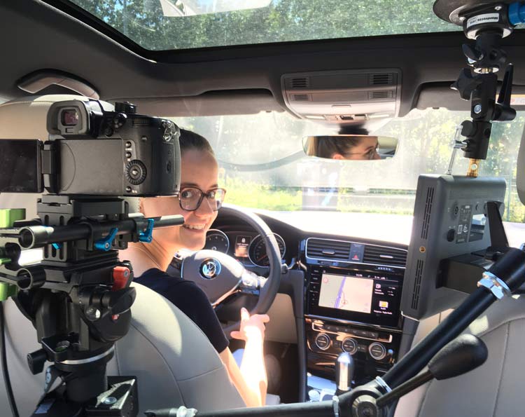 Filmproduktion & Videoproduktion 7 Autofahraufnahmen von der Videoproduktion 52Gradfilm aus Hannover. die Fahrerin schaut Richtung Kamera. Vor ihr ist eine Kamera mit spezial Filmepuipment im Auto aufgebaut.