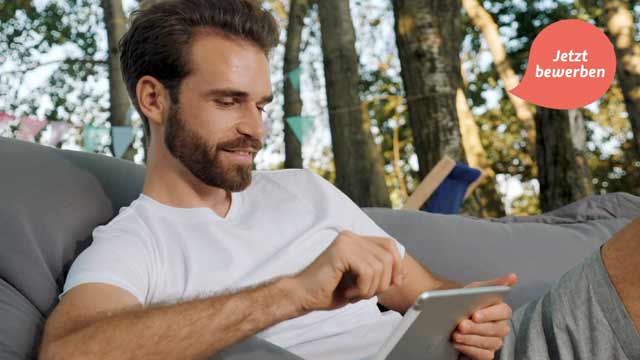 Junger bärtiger Mann sitzt im Sitzsack in der Natur und arbeitet am Tablet – Titelbild eines Recruitingvideos von 52° Film, Filmproduktion Hannover